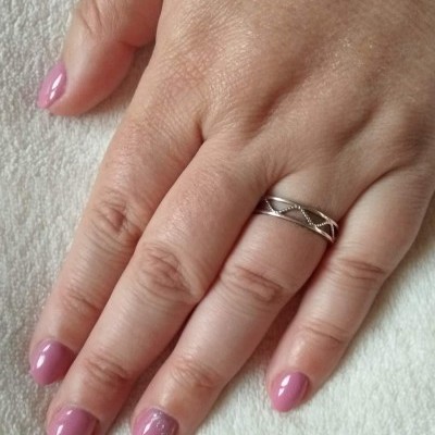 Mão feminina com unha pintada de verniz cor rosa claro e aliança de prata