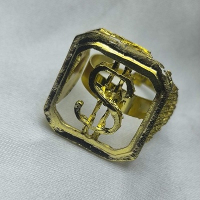 Anel dourado com símbolo de cifrão sobre tecido cinzento claro