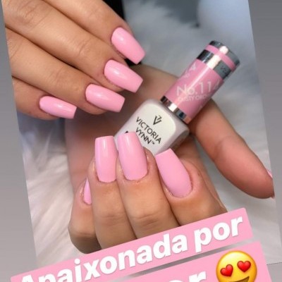 Mãos femininas com unhas cor-de-rosa claro segurando frasco de verniz Victoria Vynn Nº 11