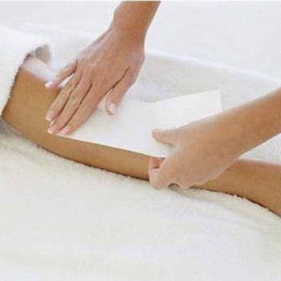 Aplicação de faixa de depilação numa perna feminina sobre toalha branca