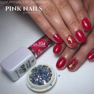 Mãos com unhas vermelhas e decoração de glitter ao lado de frasco de verniz e glitter aberto