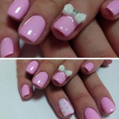 Unhas com verniz rosa claro, padrão de bolinhas rosa sobre branco e laço branco 3D com pedra