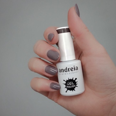 Frasco branco de verniz gel Andreia Professional com mão segurando e unhas cinza