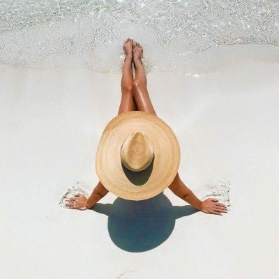 Pessoa de chapéu de palha na praia com areia branca e água transparente