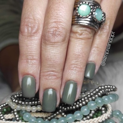 Mão feminina com unhas verdes segurar pulseiras de contas e anel com pedras verdes