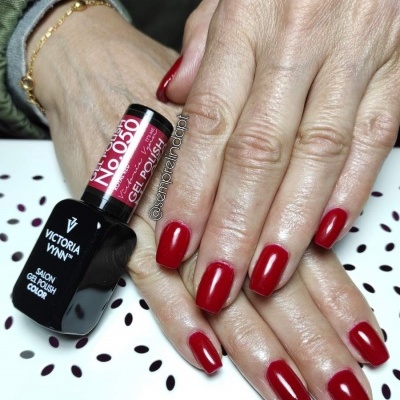 Mãos com unhas pintadas de verniz gel vermelho e frasco de verniz Victoria Vynn