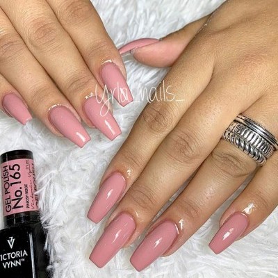 Mãos femininas com unhas de gel cor de rosa mate e frasco de verniz ao lado