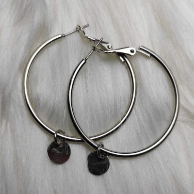 Brincos de argola em metal prateado com pendente redondo liso sobre superfície branca peluda