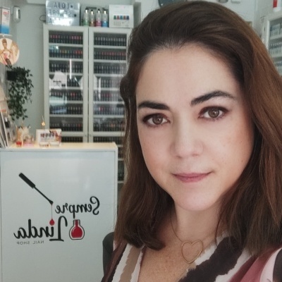 Mulher dentro de loja de unhas com receção branca e prateleiras com vernizes