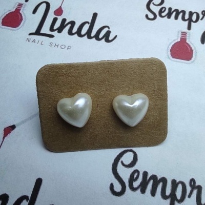 Brincos em forma de coração perolados num cartão castanho sobre fundo branco com texto em rosa e preto.