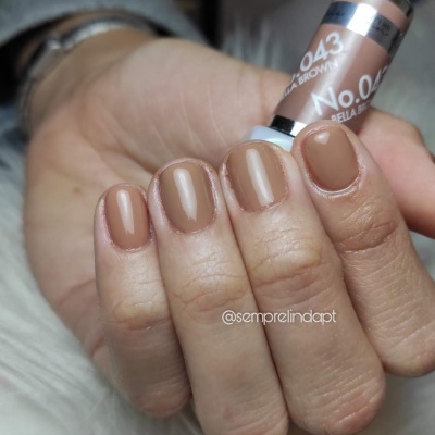 Mãos com unhas pintadas de castanho creme segurando frasco de verniz