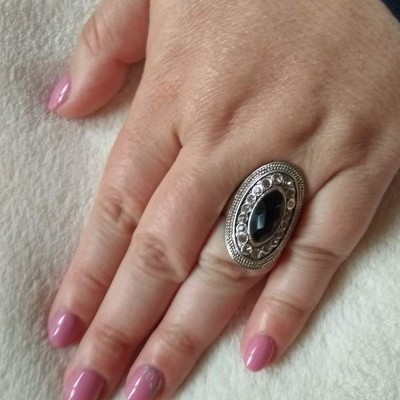 Anel oval prateado com pedra preta na mão feminina de unhas cor-de-rosa sobre tecido branco