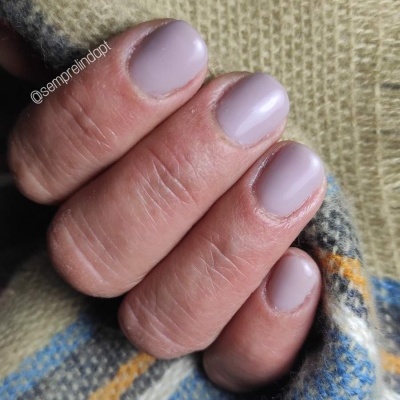 Unhas pintadas de lilás fosco segurando tecido de lã xadrez azul e amarelo