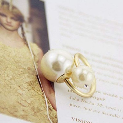 Brincos dourados com pérolas e cristal sobre página de revista com texto e imagem desfocada