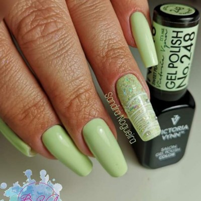 Unhas pintadas com verniz gel verde e uma decorada com glitter, junto a dois frascos de verniz gel.