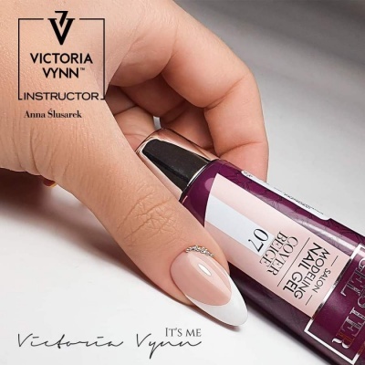 Mão segurando tubo de verniz Victoria Vynn com rótulo branco, roxo e rosa