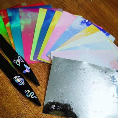 Cartões metálicos coloridos e unhas postiças pretas com desenhos prateados sobre madeira.