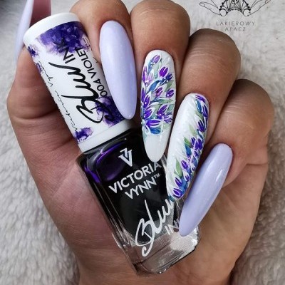 Unhas decoradas com verniz lilás e flores em violeta segurando frasco de verniz Victoria Vynn Blue 004 VIOLA