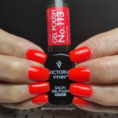 Unhas pintadas com verniz gel vermelho vibrante segurando frasco Victoria Vynn