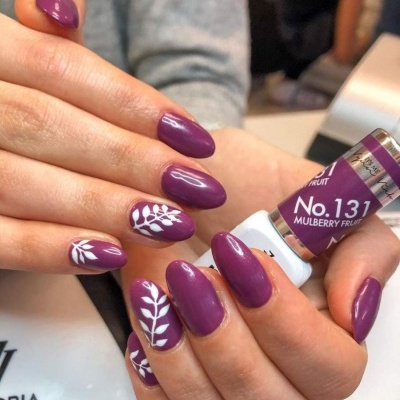 Unhas pintadas em roxo com detalhes brancos segurando esmalte No.131 Mulberry Fruit.