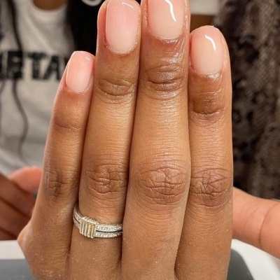 Mão feminina com unha rosa claro e anel prateado com detalhes dourados