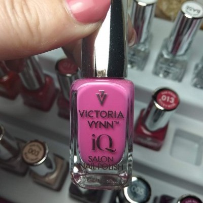 Frasco de verniz para unhas rosa Victoria Vynn com tampa prateada e mão segurando.