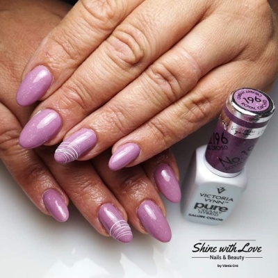 Mãos com unhas pintadas de verniz roxo cintilante e detalhes brancos, ao lado de frasco de verniz roxo e branco da marca Victoria Vynn Pure.