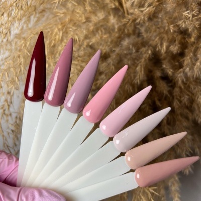 Amostras de verniz de unhas em vários tons de rosa e vermelho em fundo de plantas secas.