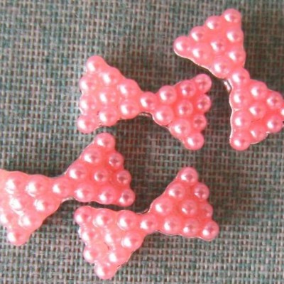 Quatro apliques em forma de laço com pérolas cor-de-rosa sobre tecido cinza