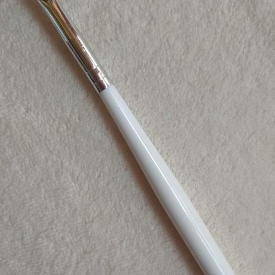 Pincel de maquilhagem com cabo branco e cerdas roxas em fundo branco