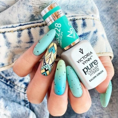 Manicure com verniz azul esverdeado mate e desenho étnico colorido segurando frasco de verniz