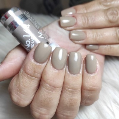 Mãos com unhas quadradas pintadas de verniz taupe brilhante segurando frasco de esmalte