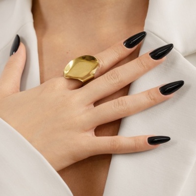 Mão feminina com anel dourado grande e unhas pretas em casaco branco