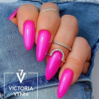 Mão com unhas longas cor de rosa e anéis com brilhantes sobre roupa de ganga azul