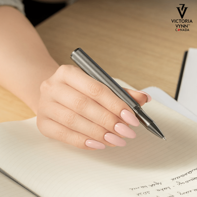Mão segurando caneta metálica sobre caderno pautado e logo Victoria Vynn Canada
