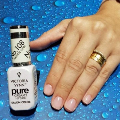 Esmalte Victoria Vynn Pure Creamy Hybrid No.108 Natural Ivory com mão feminina e unhas pintadas rosa claro sobre superfície azul com gotas d'água