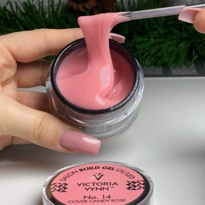 Gel de construção para unhas Victoria Vynn No. 14 Cover Candy Rose em frasco aberto, textura cremosa de cor rosa, tampa rosa com texto, fundo com decoração verde e pinha
