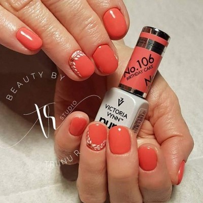 Unhas curtas pintadas de cor coral com decoração branca tribal, segurando frasco de esmalte Victoria Vynn nº 106 Birthday Cake