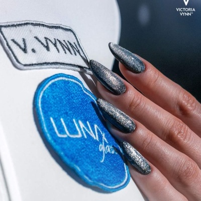 Mãos com unhas prateadas segurando bolsa branca com distintivos azul e branco