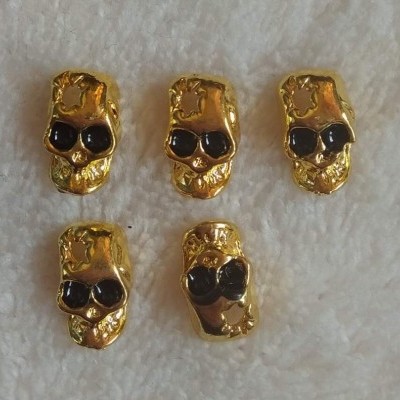 Cinco contas douradas em forma de caveira com olhos pretos sobre tecido branco felpudo