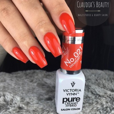 Mão com unhas vermelhas brilhantes segurando frasco de verniz Victoria Vynn