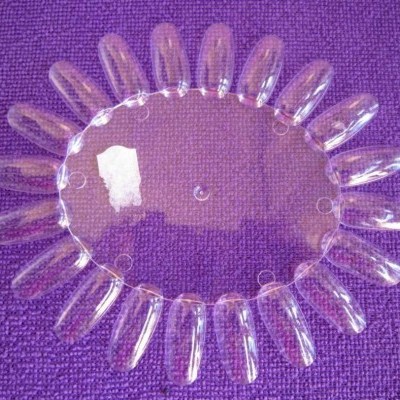Mostruário de unhas artificiais transparentes para amostras de verniz, sobre tecido roxo.