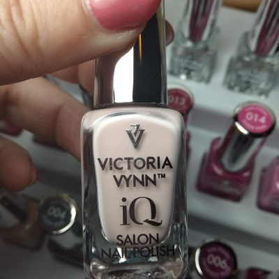 Frasco de verniz para unhas VICTORIA VYNN IQ SALON cor rosa claro com tampa prateada segurado por mão com unha pintada de rosa forte
