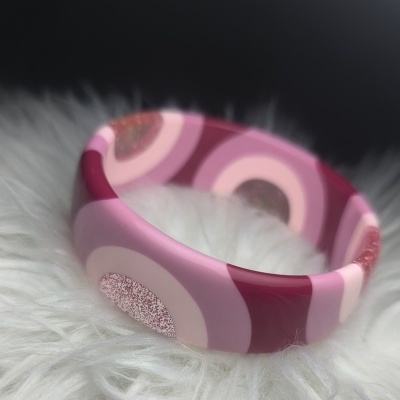 Pulseira rígida rosa com padrão de círculos e glitter sobre fundo branco macio
