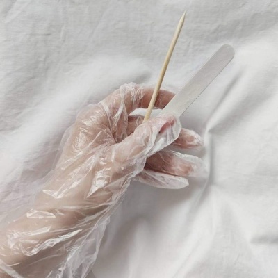 Mão com luva plástica segura palito de madeira e espátula de plástico