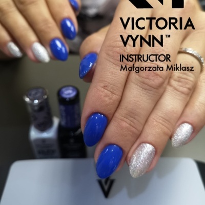 Unhas com verniz azul e prateado brilhante sobre mãos femininas com anel prateado.