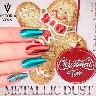 Unhas com verniz metálico verde-azulado e vermelho segurando figura de pão de gengibre dourada em fundo branco