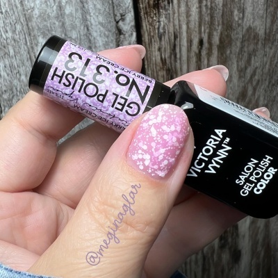 Frasco de verniz gel preto e pequeno frasco rosa com bolinhas brancas segurados por uma mão com unha decorada rosa e brancas