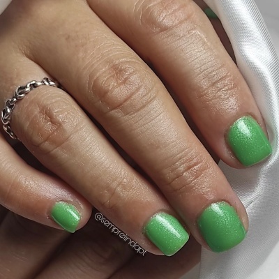 Mão com unhas verdes cintilantes e anel prateado sobre tecido branco