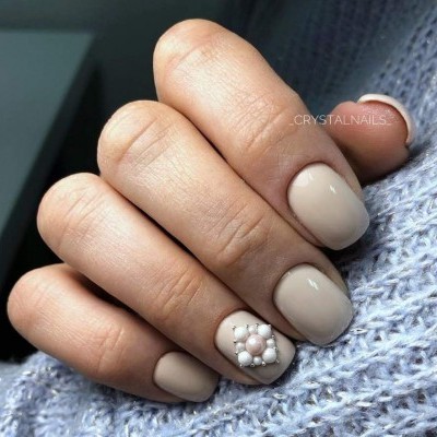 Unhas curtas com verniz bege claro e decoração com pérolas brancas numa unha